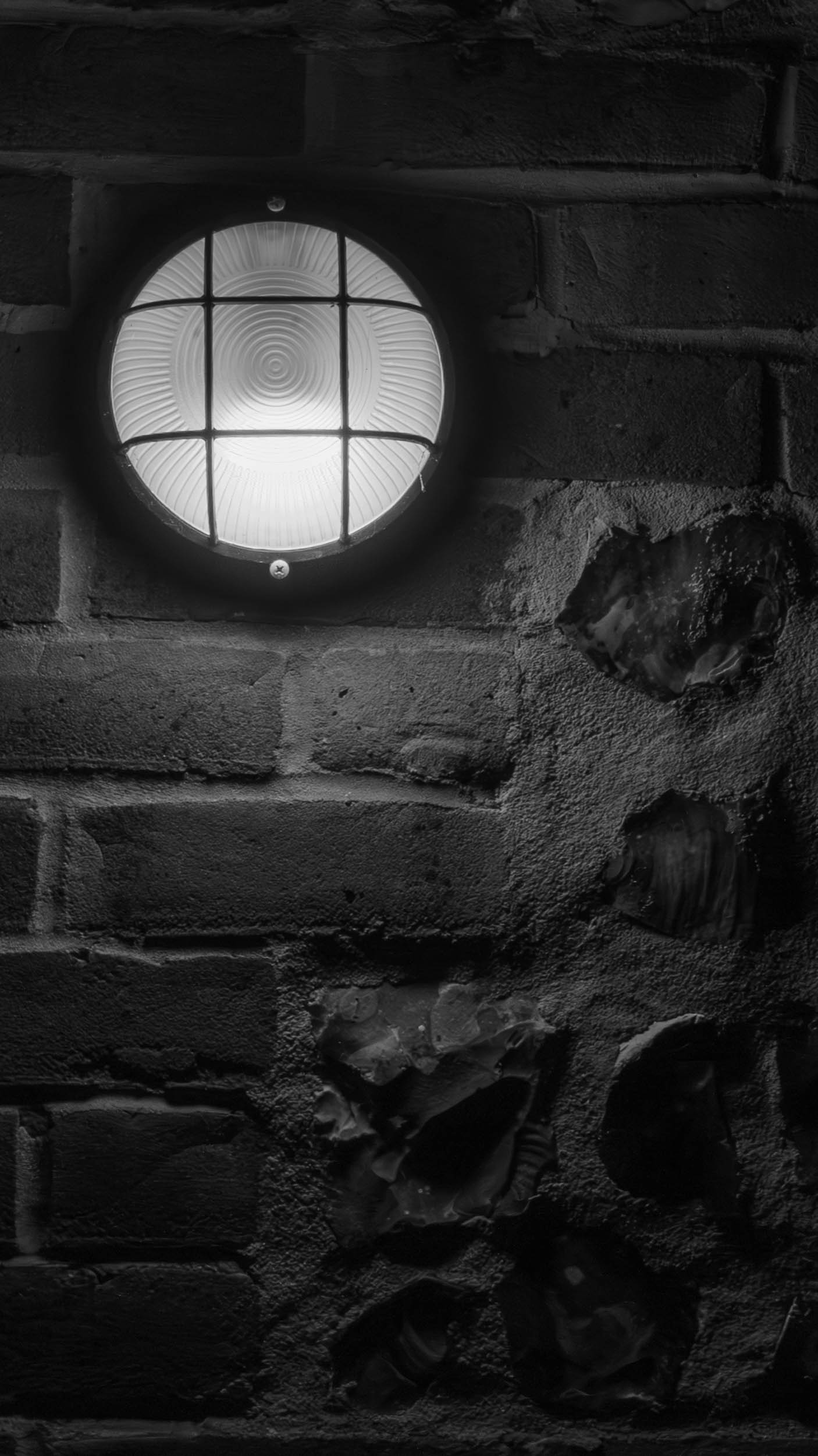 Black and White image of industrial-tyle outside light on a brick and flint wall.